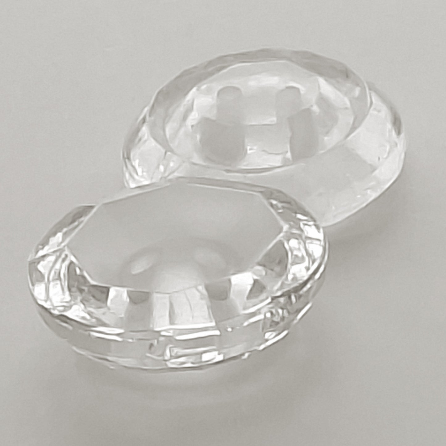 Side view of two clear glass buttons with frosted centers, one positioned right-side up and the other facing down, showing the thickness and outer shape of the rim.