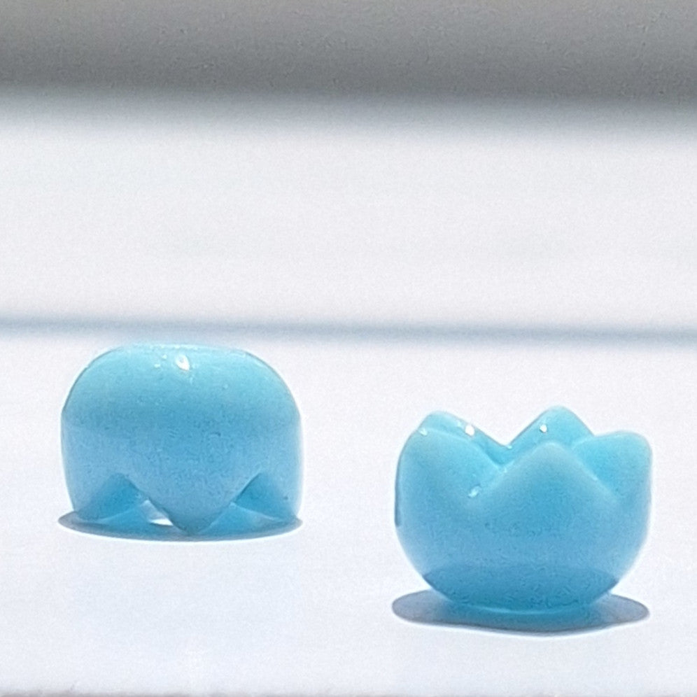 Two turquoise glass spacer beads with a tulip-style cut one face up and the other face down.