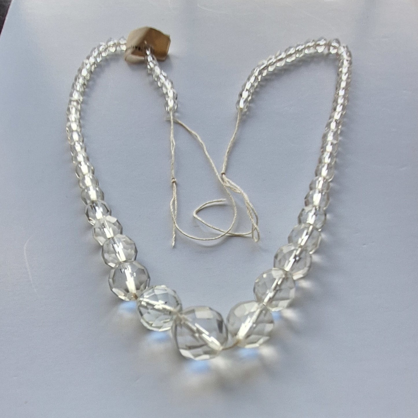 Clear crystal glass necklace with faceted graduated beads, temporarily strung without clasp, shown laid flat