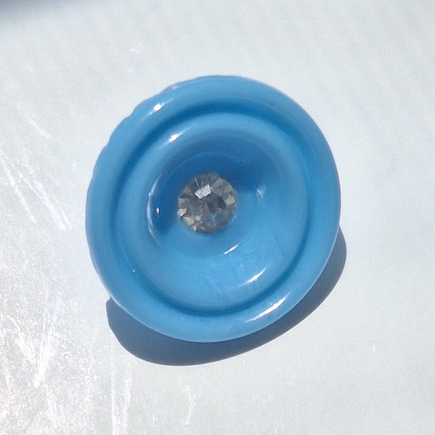 Blue plastic cup-shaped shank button with clear glass rhinestone center, 18mm.