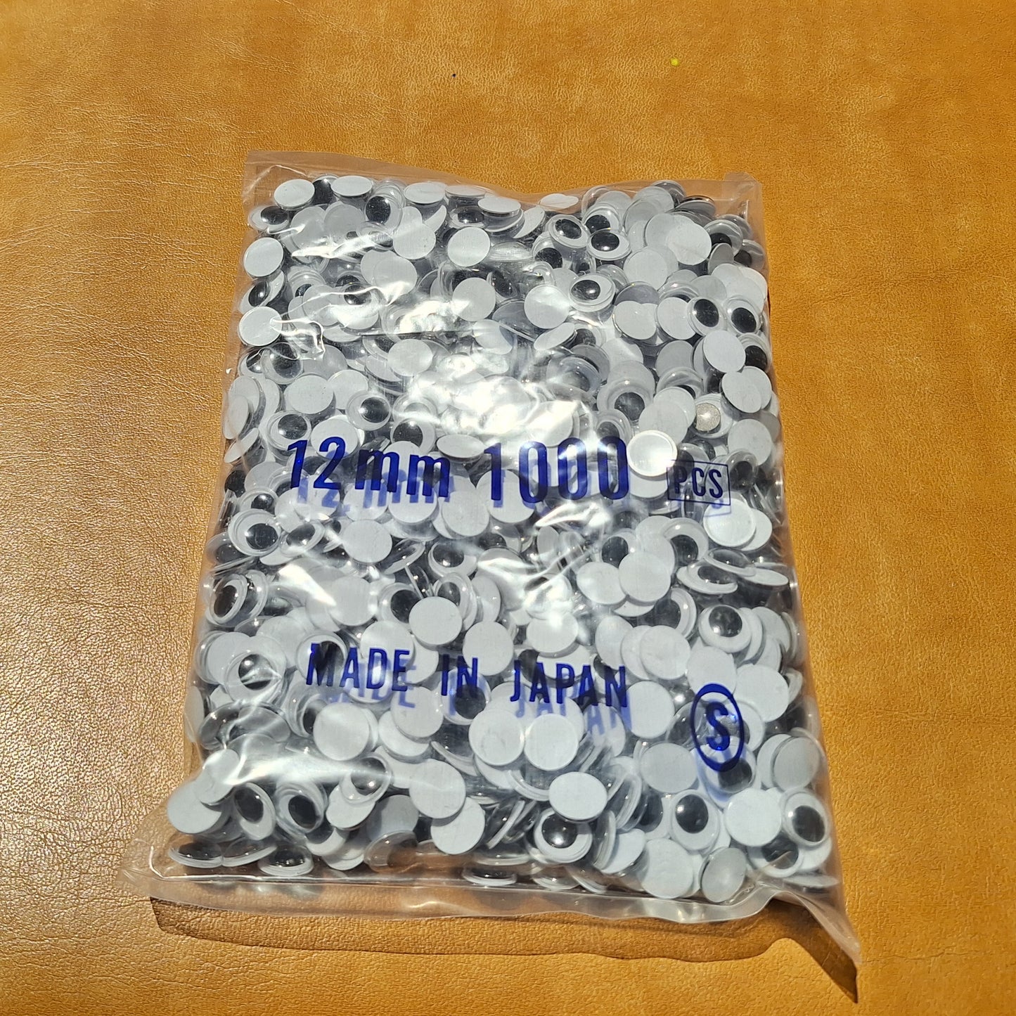 Bag of 1000 12mm paste-on googly eyes with a flat black pupil made in Japan.