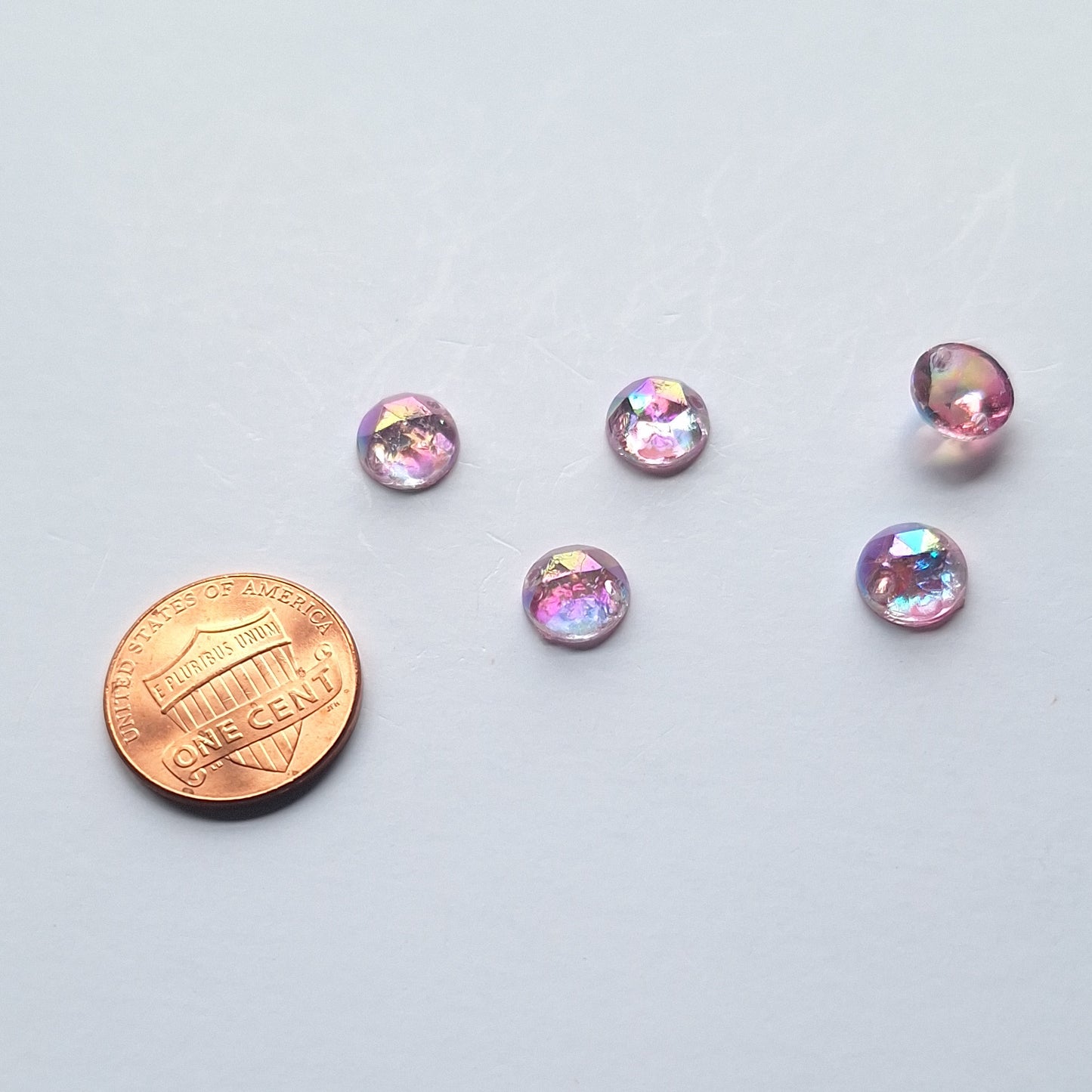 Amethyst AB round faceted cabochons arranged in a group of five, with one flipped to show the two-hole sew-on back; penny included for scale.