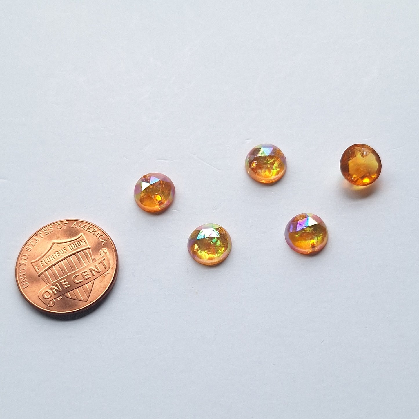 Topaz AB round faceted cabochons arranged in a group of five, with one flipped to show the two-hole sew-on back; penny included for scale.