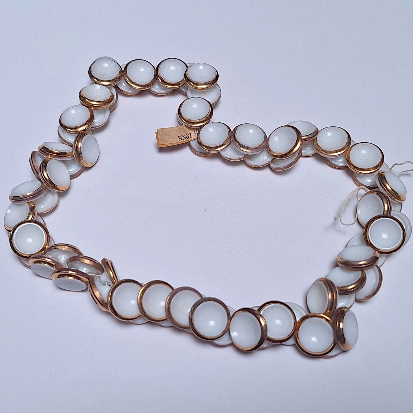 group photo of white glass button with gold luster edge and tag showing U.S. Zone origin