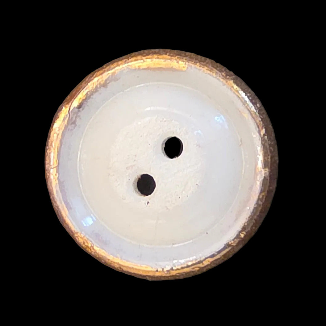 Back of white two-hole glass button with raised faceted gold luster rim.