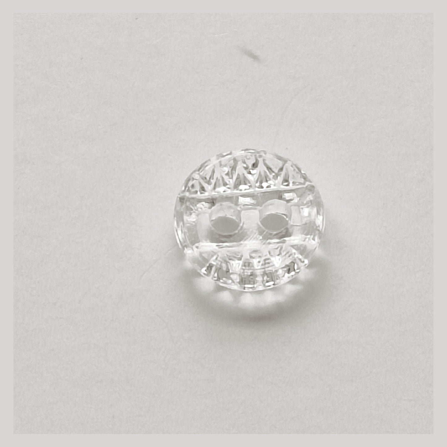 Small crystal glass button with smooth concave face, central clear band, and two-hole construction, photographed from above.