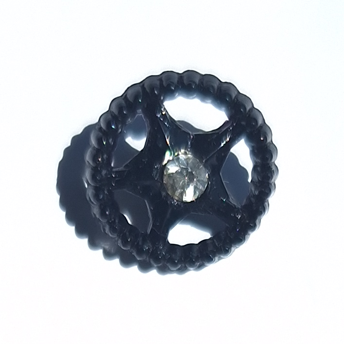 Black star-in-wheel plastic button with openwork rim and central glass rhinestone, 14mm.