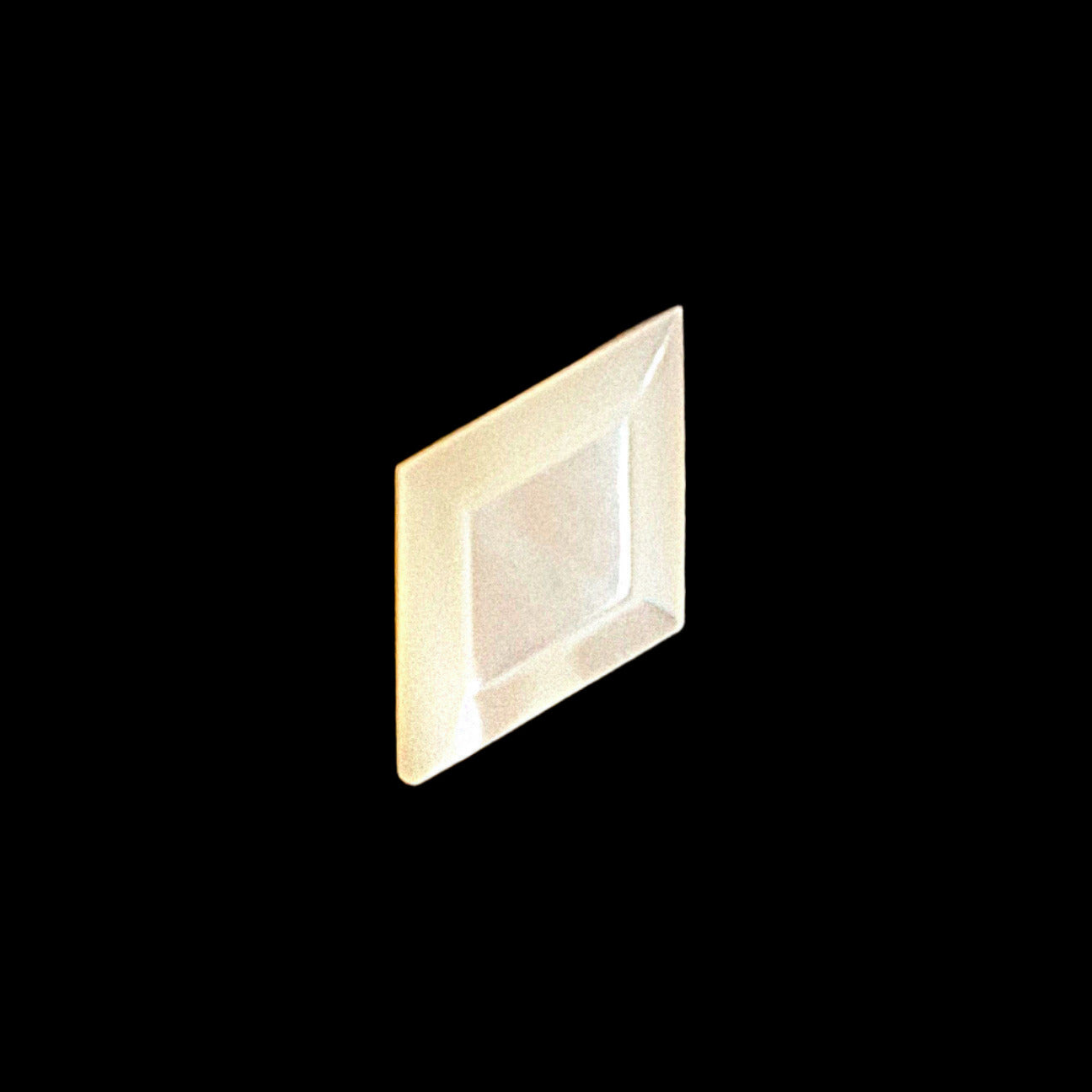 Diamond-shaped carved shell button with a raised faceted center panel, shown angled on a dark textured background.