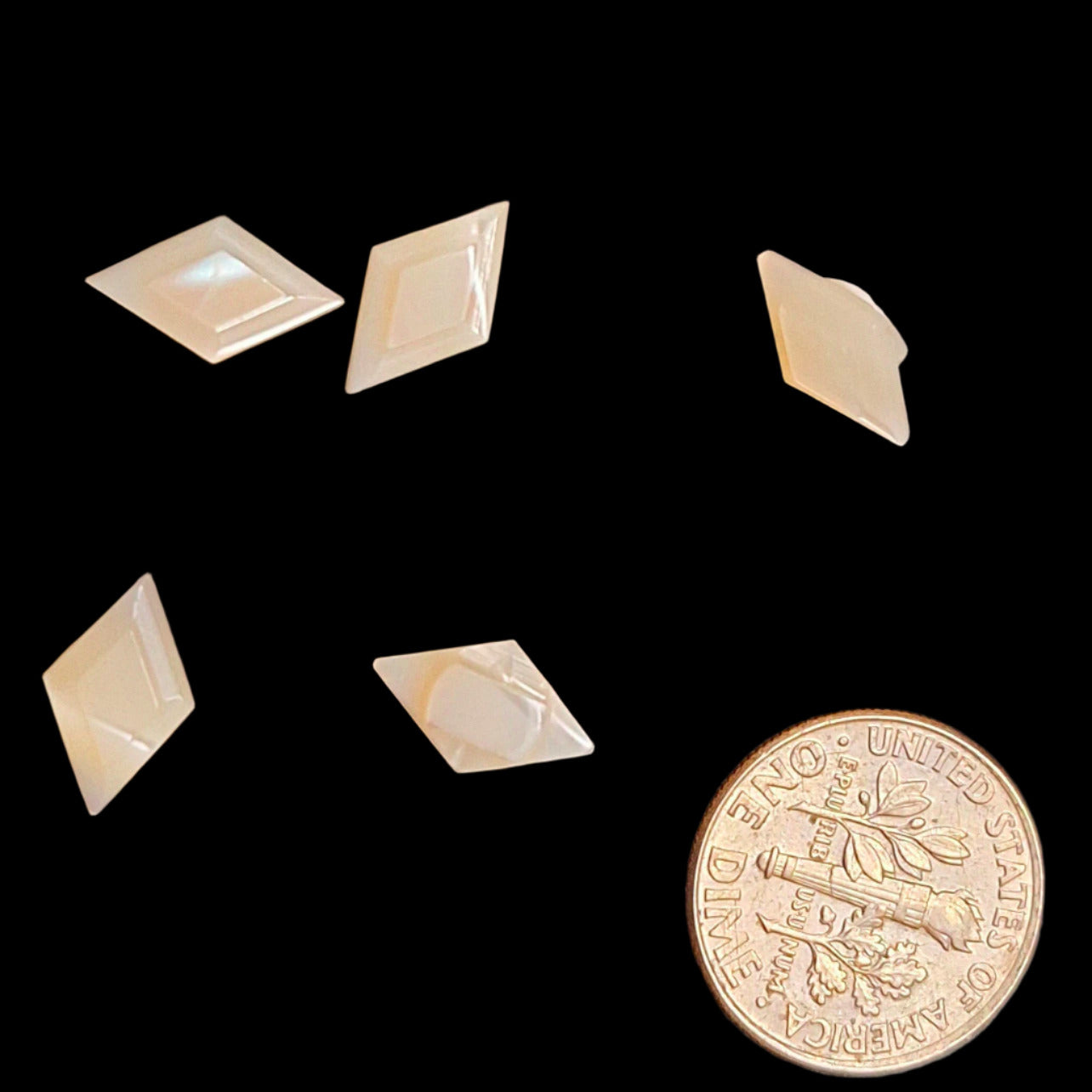 Multiple diamond-shaped carved shell buttons arranged near a U.S. dime for scale, highlighting size and natural shell luster.