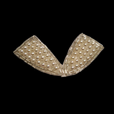 Bow-shaped applique with an outline of bugle beads and imitation pearls covering each region on a black background