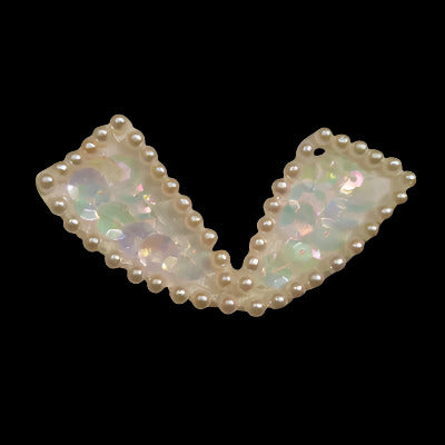 Bow-shaped applique with an outline of pearl beads and covered with iridescent sequins, on a black background