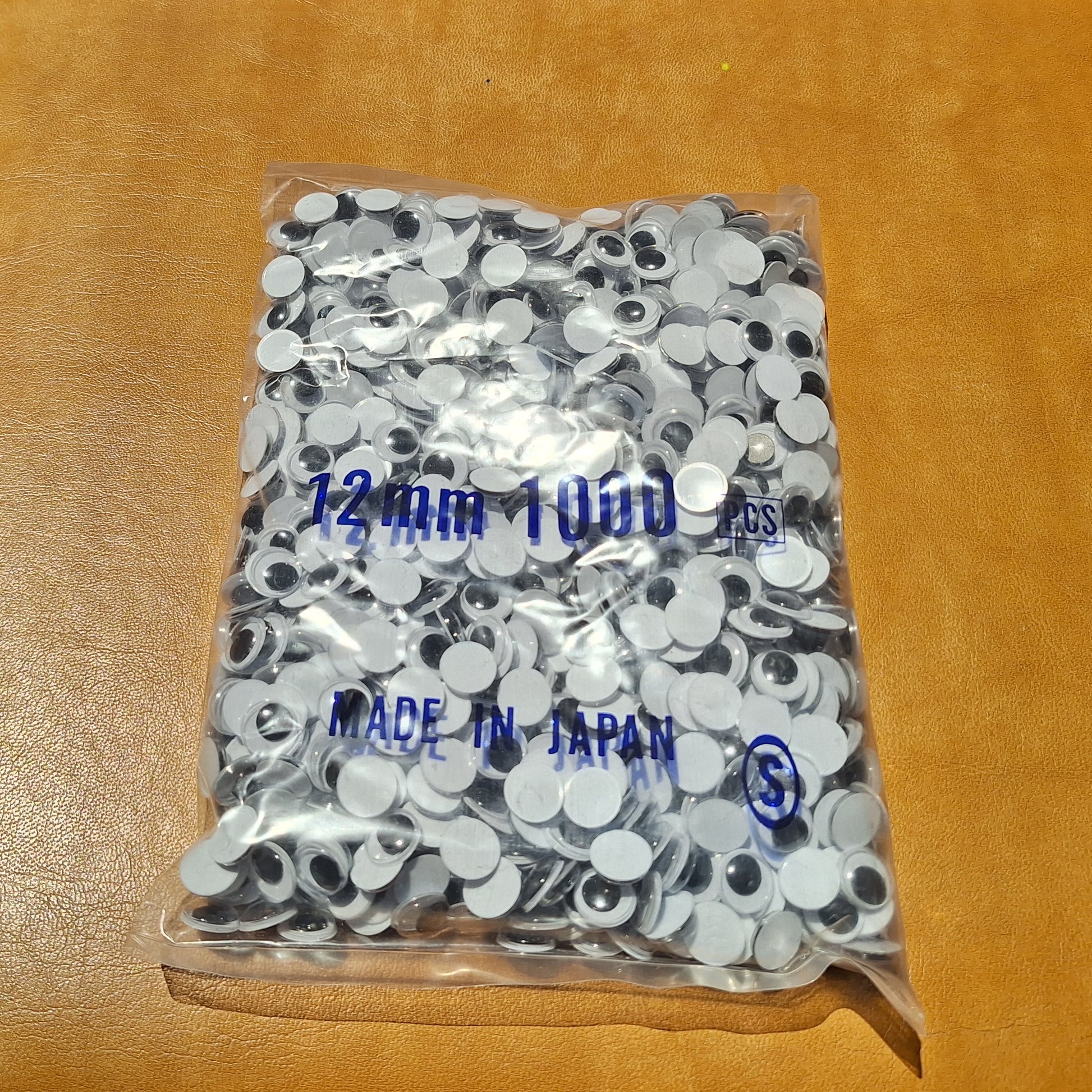 Bag of 1000 12mm paste-on googly eyes with a flat black pupil made in Japan.