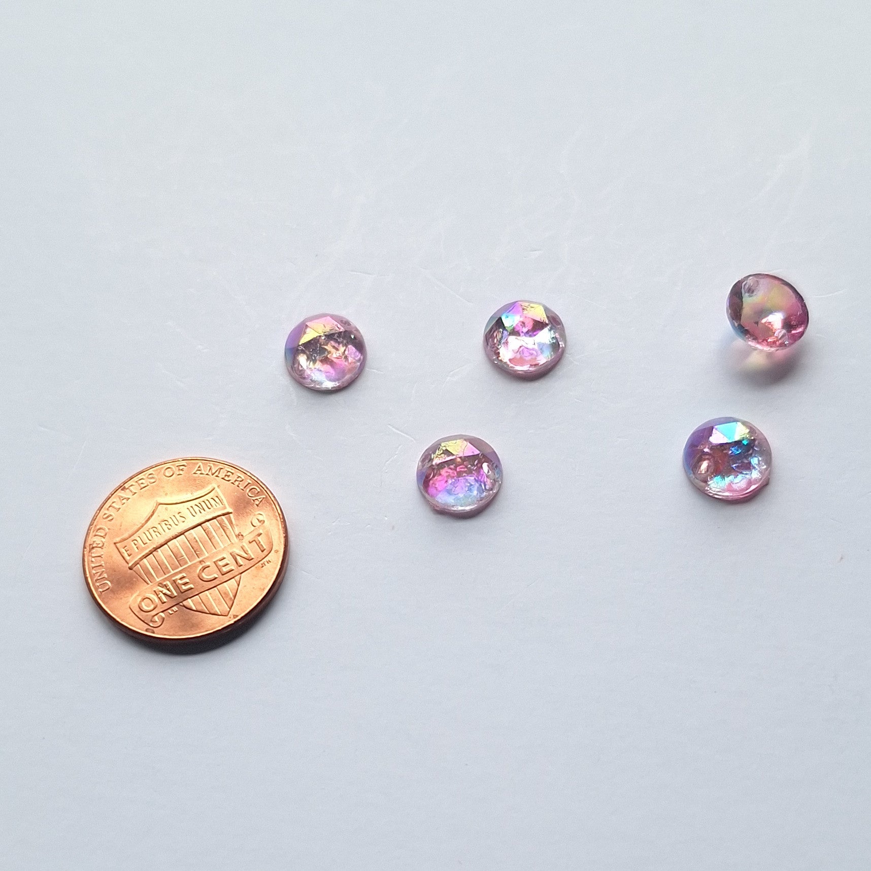 Amethyst AB round faceted cabochons arranged in a group of five, with one flipped to show the two-hole sew-on back; penny included for scale.