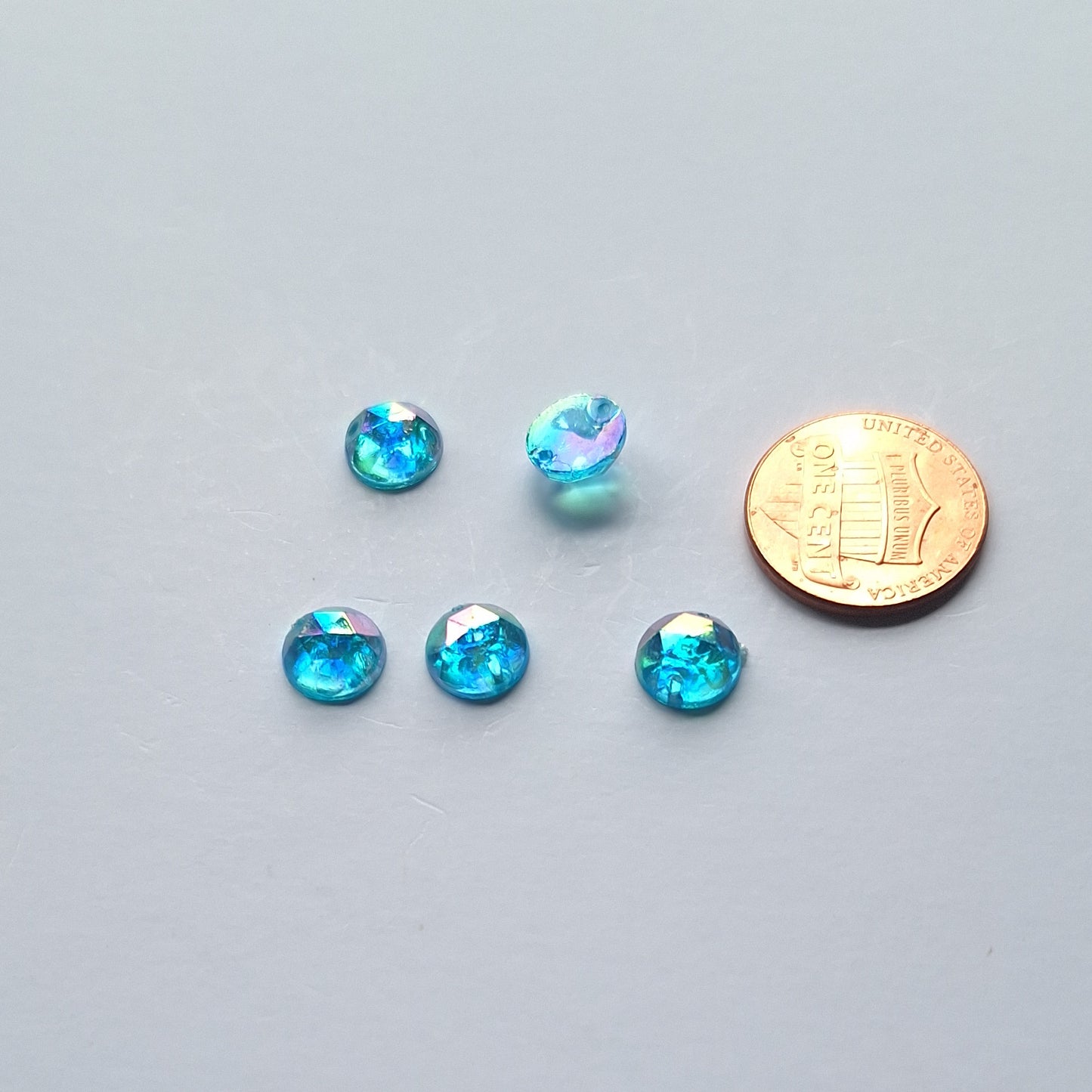 Aqua AB round faceted cabochons arranged in a group of five, with one flipped to show the two-hole sew-on back; penny included for scale.