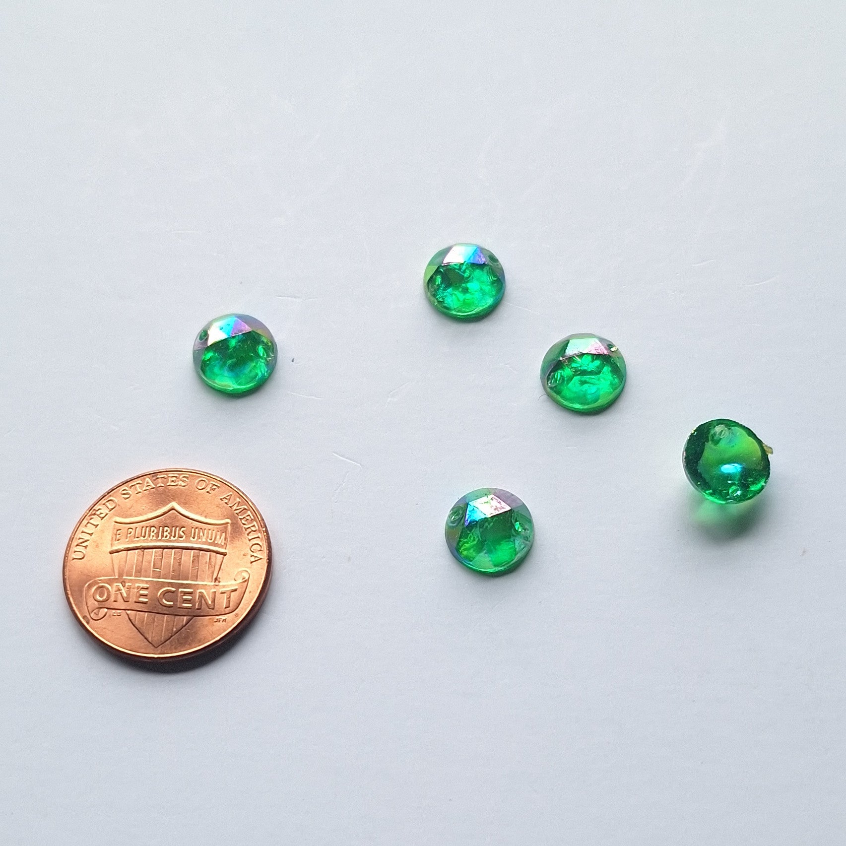 Emerald AB round faceted cabochons arranged in a group of five, with one flipped to show the two-hole sew-on back; penny included for scale.