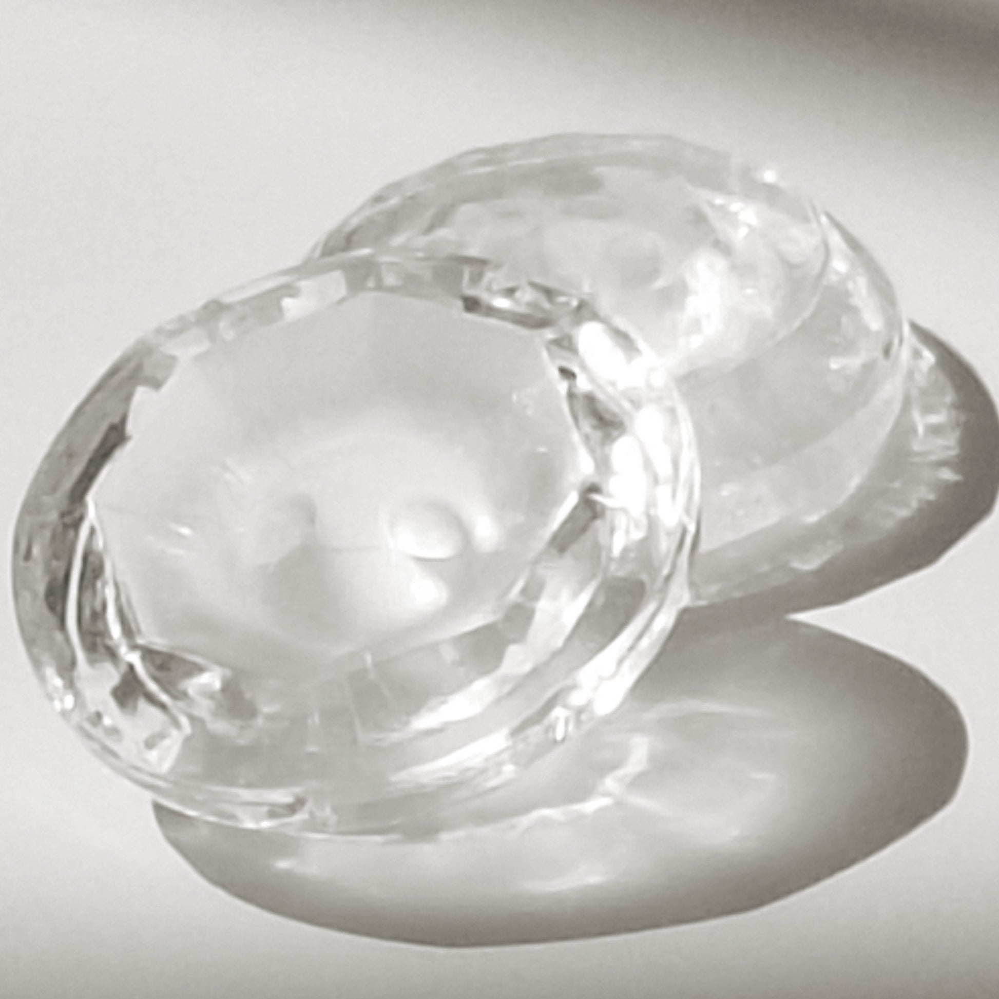 Two clear glass buttons with frosted centers, one facing up and leaning against another facing down, photographed in strong directional light that creates pronounced reflections.