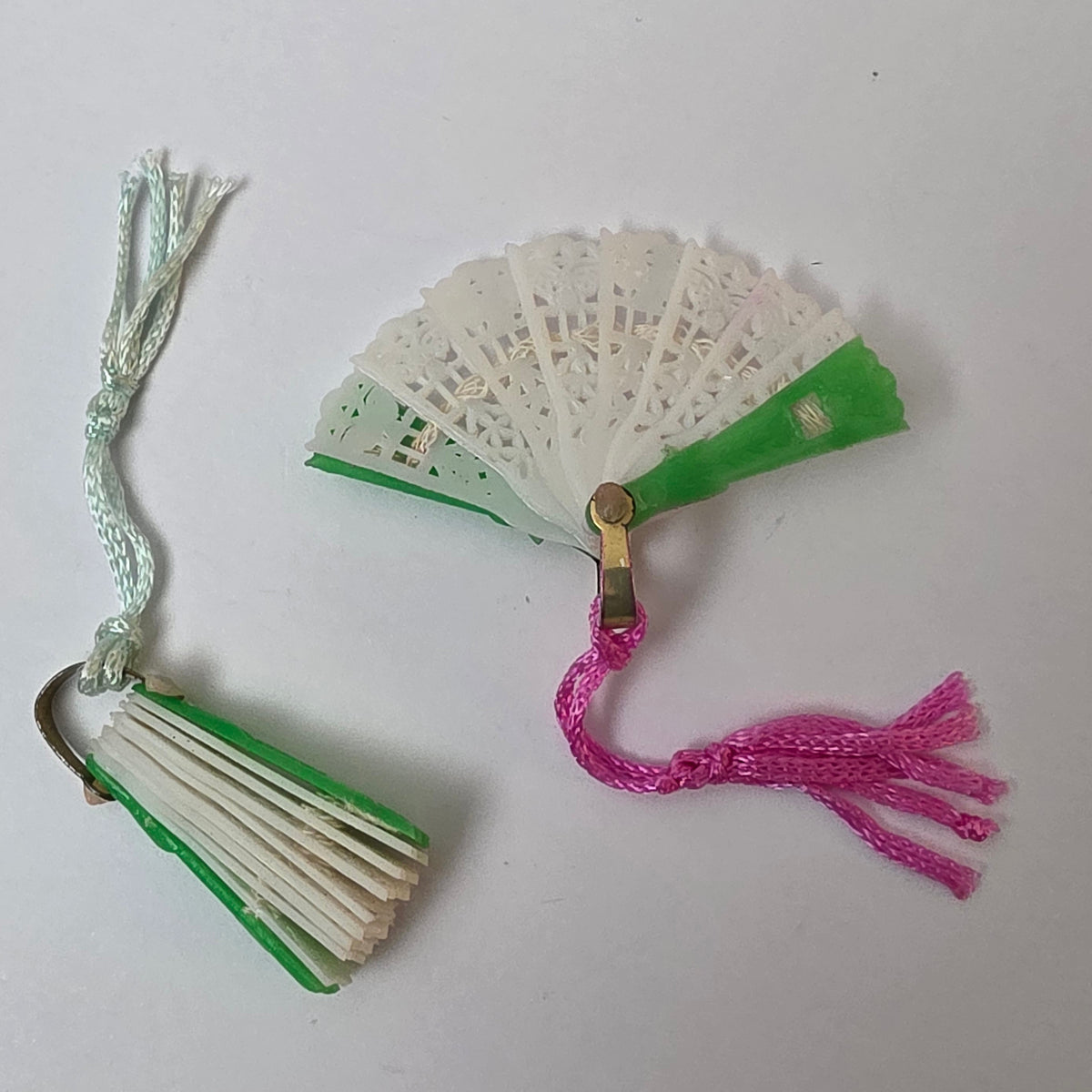 Vintage miniature green plastic folding fan shown open and closed, with decorative white center panels and silk tassels.
