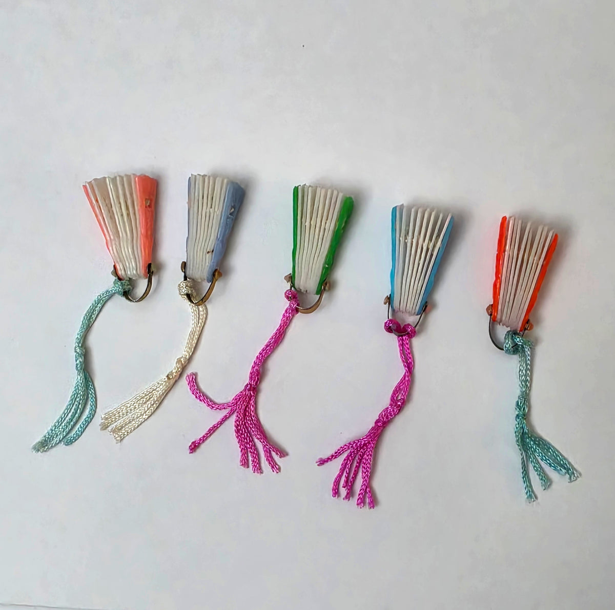 Five vintage miniature plastic folding fans shown closed in pink, blue, green, aqua, and red, with assorted silk tassel colors.