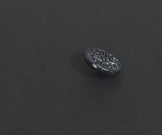 Video of a gunmetal metalized button with raised starburst design and geometric detailing radiating from a central flower, shank back, 18mm.