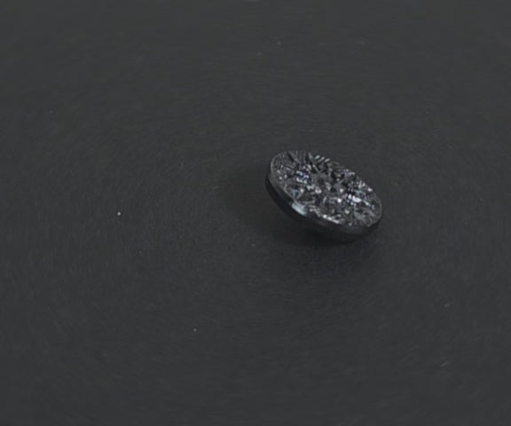 Video of a gunmetal metalized button with raised starburst design and geometric detailing radiating from a central flower, shank back, 18mm.